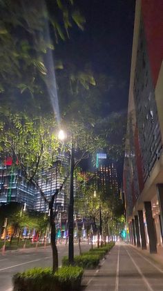 an empty city street at night with tall buildings and trees in the foreground,