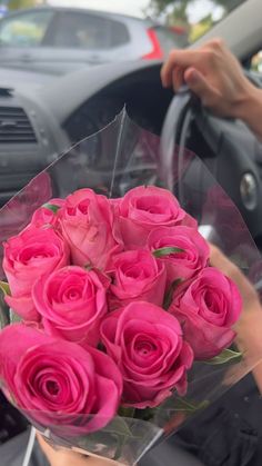 a bunch of pink roses sitting in the passenger seat of a car with someone's hand on the steering wheel