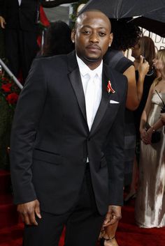 a man in a tuxedo standing on a red carpet with an umbrella over his head