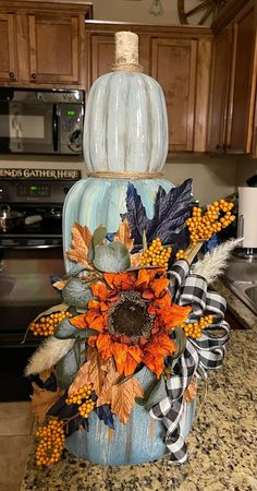 a blue pumpkin decorated with fall leaves and sunflowers sits on a kitchen counter