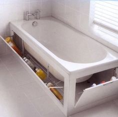 a bath tub sitting under a window next to a shelf filled with bottles and containers