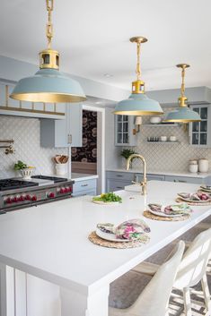 a white kitchen with blue cabinets and gold pendant lights above the island countertop is featured on instagram