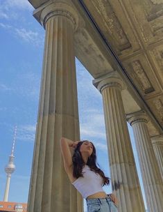 a woman standing in front of some pillars with her hands behind her head and looking up at the sky