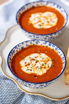 two bowls of tomato soup on a white plate with breadsticks and blue napkin