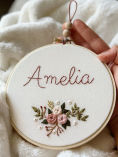 someone is holding up a hand embroidered name ornament with flowers and leaves on it