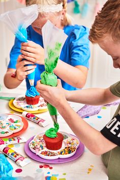 two children are painting cupcakes with green icing