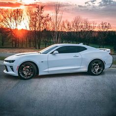 a white chevrolet camaro is parked on the side of the road in front of some trees