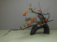 a sculpture made out of branches and flowers on top of a white table with grey background