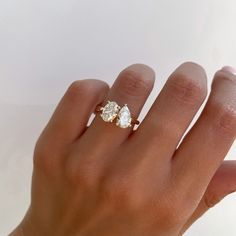 a woman's hand holding a three stone ring with two pear shaped diamonds on it