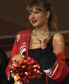 a woman in a red and black outfit is holding a christmas ornament while looking at the camera