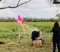 two people sitting on a hay bale in the middle of a field with a pink flower