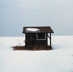 an outhouse in the middle of nowhere with snow on the roof and grass around it