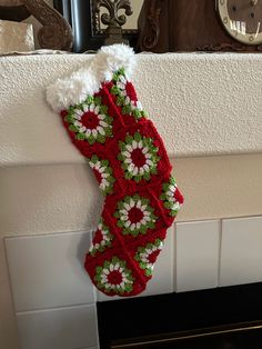 a knitted christmas stocking hanging from a fireplace mantel with a clock in the background