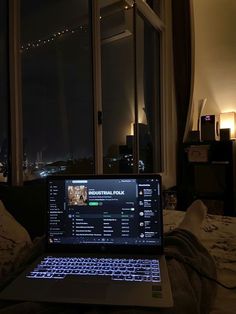 an open laptop computer sitting on top of a bed in front of a large window