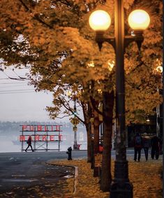 people are walking on the sidewalk near some trees and street lights with an orange sign in the background