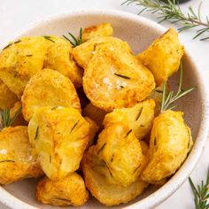 a white bowl filled with fried potatoes covered in cheese and rosemary sprinkled on top