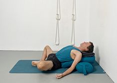 a man laying on a mat in front of two ropes hanging from the wall, with his eyes closed