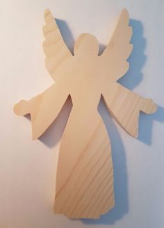 an unfinished wooden angel ornament on a white surface with the wings spread out