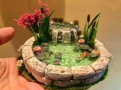 someone is holding a miniature pond with water and flowers