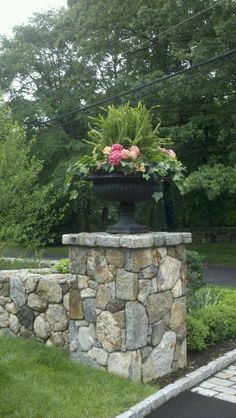 a large planter with flowers in it on top of a stone wall next to a paved road