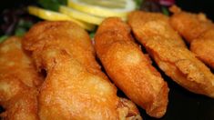 some fried food on a black plate with lemon wedges and salad in the background