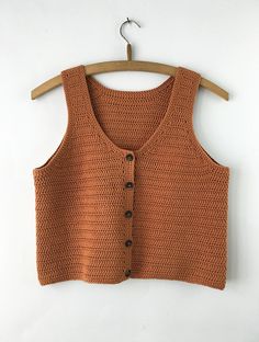 an orange knitted vest hanging on a wooden hanger