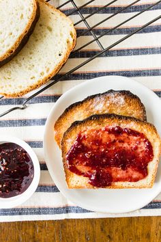 two slices of bread with jam on them next to a bowl of jelly and spoons