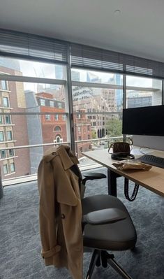 an office with a coat hanging on the wall and a desk in front of a large window