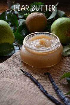 a jar of pear butter sitting on top of a table next to some apples and leaves