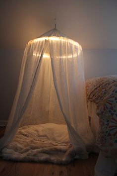 a bed with a white canopy over it in a room next to a pillow on the floor