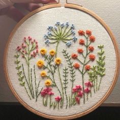 a hand holding a hoop with flowers on it and the embroidery is done in different colors