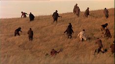 a group of people walking up a hill in the middle of an open field with tall grass