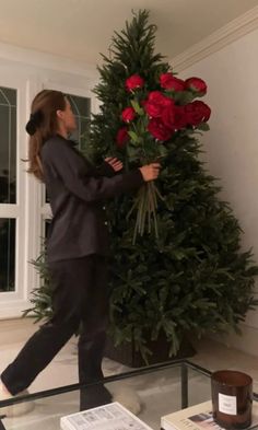 a woman is placing flowers on top of a christmas tree