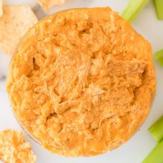 a bowl of dip surrounded by celery and crackers on a white surface