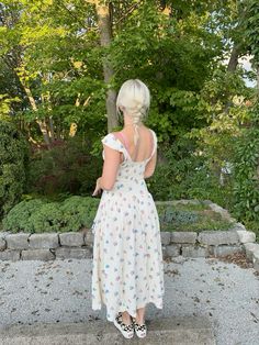 a woman in a white dress is standing on some steps and looking at the trees