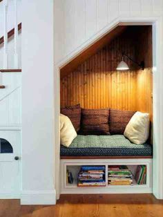 an open space under the stairs is filled with books and magazines as well as a built - in bench for reading