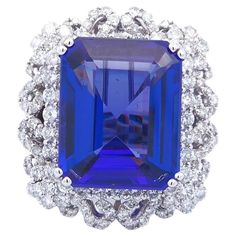 Luxury, at the right price. This unique ring has a 23.64 carat total weight. The center stone is a tanzanite emerald cut weighing 19.89 carats. Surrounding the tanzanite are 3.75 carats of round cut diamonds set in 18K white gold. This ring is set at a size 6 3/4. This stunning ring features tanzanite set and arranged in the center and surrounded by diamonds. All of these sparkling stones are surrounded in elegant and classic 18 karat white gold, creating a truly amazing azure gemstone diamond ring that is sure to turn heads at your next event. The Jewelry Exchange offers captivating factory direct gemstones at the guaranteed lowest prices on the market, saving you up to 80% compared to other retailers! Gemstone Diamond Ring, Tanzanite Pendant, Tanzanite Diamond Ring, Tanzanite Stone, Tanzanite Diamond, Types Of Diamonds, Tanzanite Ring, Modern Ring, Unique Ring