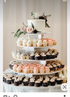 a three tiered cake with cupcakes and flowers on the top is surrounded by other desserts