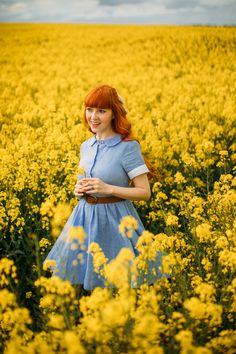 a woman with red hair standing in a field of yellow flowers and smiling at the camera