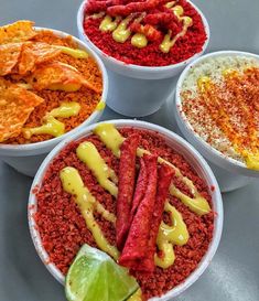 four bowls filled with different types of food on top of a gray table next to two lime wedges