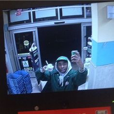 a man holding up his cell phone while standing in front of a convenience store window