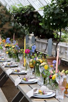 a long table is set with flowers and candles for an outdoor dinner or party in a greenhouse