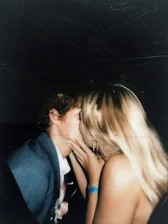 two people are kissing each other in front of a black background and one person is wearing a blue blazer