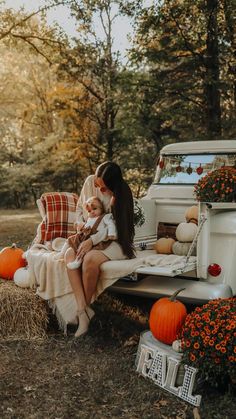 a woman sitting on the back of an old truck with pumpkins and hay bales