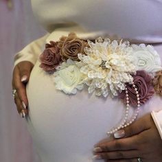 a pregnant woman wearing a flower belt with pearls and beads on the waist, holding her belly