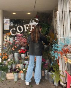 a woman standing in front of a flower shop with lots of potted flowers on display