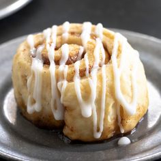 a cinnamon roll with icing sitting on top of a metal plate next to other plates