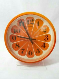 an orange clock with numbers on the front and sides, sitting on a clear acrylic stand