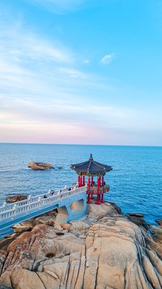 a white and red building on top of a rock next to the ocean with blue sky