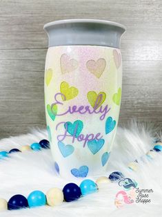 a cup with hearts painted on it sitting next to some beads